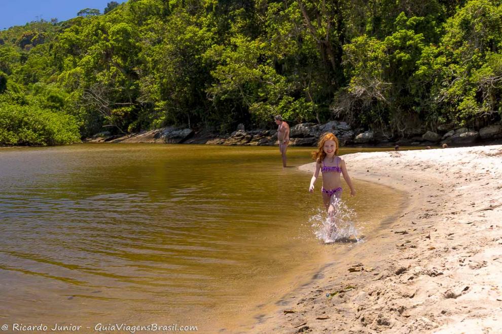 Imagem de uma criança andando na beira da piscina chutando as águas.